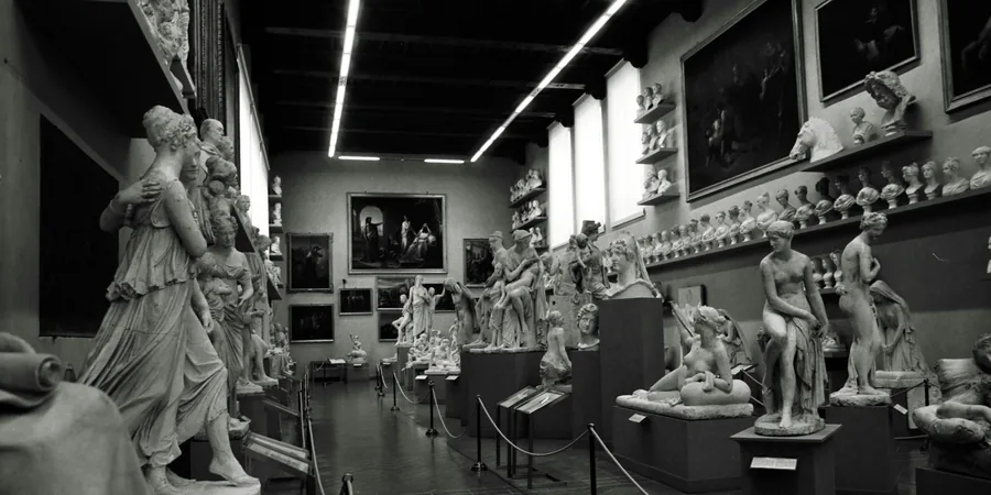 Salle de musée en noir et blanc avec statues blanches sur socles et tableaux aux murs